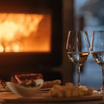 An image of two wine glasses and an appetizer in front of a fireplace